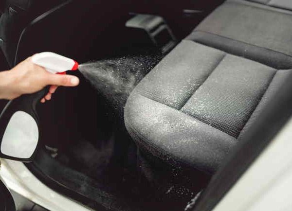 Hand spraying cleaning solution on dirty car seat