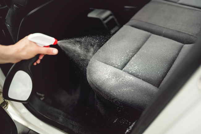 Hand spraying cleaning solution on dirty car seat